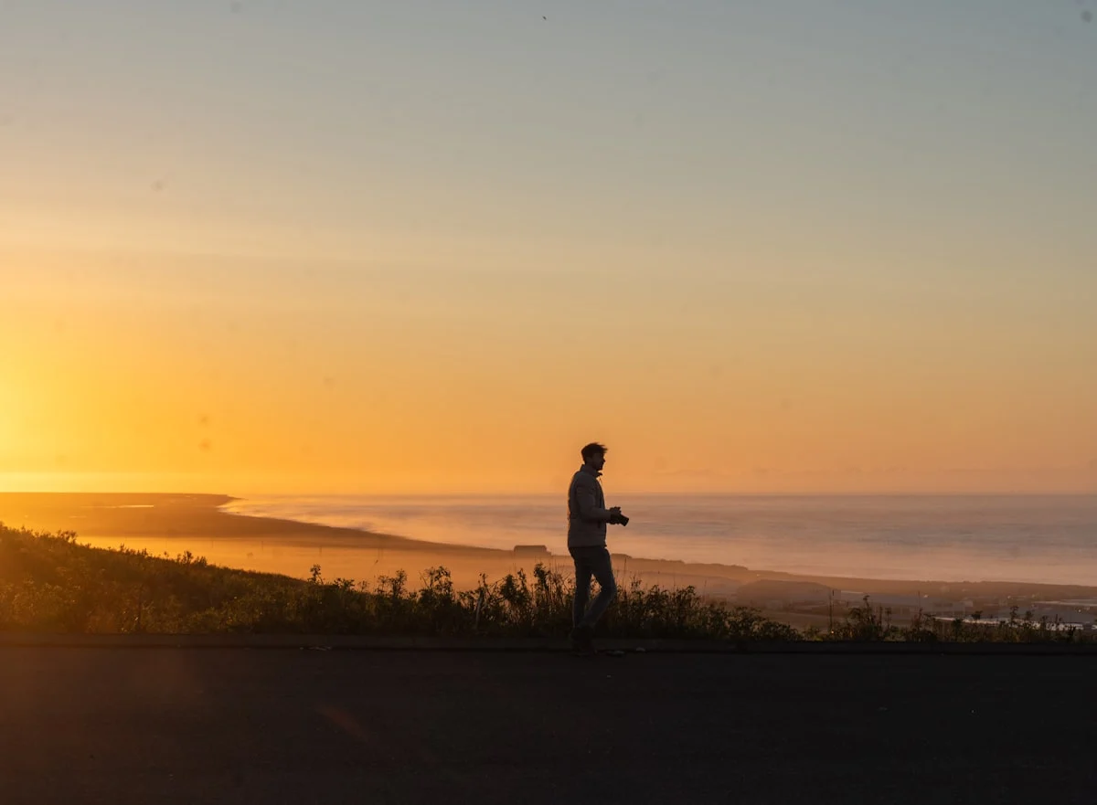 Man walking on a hill overlooking the ocean at sunset