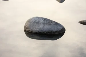 a rock in a body of water with a sky in the background
