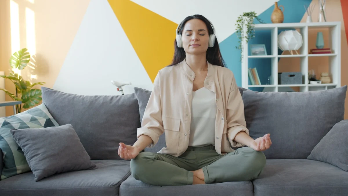 happy girl in headphones listening to music and relaxing lotus position sitting on sofa in apartment enjoying leisure time and modern technology.