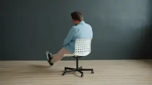 Sad young man in stylish clothing is spinning in office chair indoors in studio on dark gray background. Human emotions, people and interior concept.